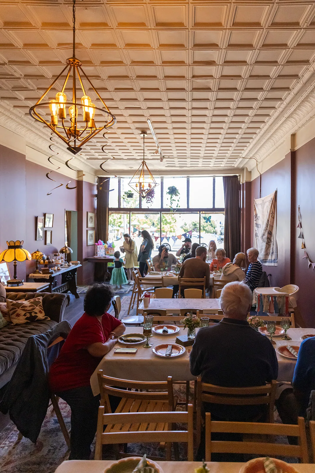 Guests seated at tables throughout the bookstore event space, under a pressed tin ceiling and pendant chandelier with tall front windows behind them